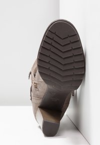 Botte en daim marron avec une surface texturée, une semelle en caoutchouc à motif en zigzag, et un talon bas et incliné. Détail de fermeture éclair sur le côté visible.