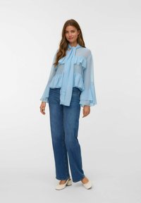 Ljusblå genomskinlig blus med lager av volanger och en knytning i halsen, matchad med hög midjad mörk denimjeans och krämfärgade blockklackar.