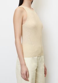Ribbet, ærmeløs top i lys beige, med rund hals og tætsiddende design. Blød tekstur med subtile syningsdetaljer langs siderne.