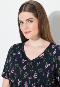 Maglia a V blu navy con motivo floreale in rosa e verde, dotata di maniche corte e dettaglio decorativo con bottone sullo scollo.