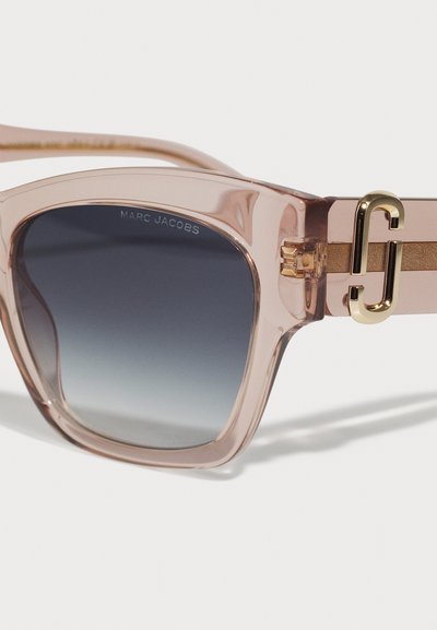 Caurskatīgas rozā saulesbrilles ar gradienta pelēkiem lēcu, ar zelta dekoru uz rāmja un zīmola nosaukumu "MARC JACOBS" iegravētu.