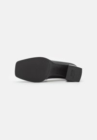 Černý vysoký podpatek s texturovanou gumovou podešví, plochým podpatkem a rovnou hranou. Minimalistický design se značením.