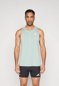 Šviesiai žalia be rankovių sportinė liemenė su apvalia iškirpte, pagaminta iš lygios medžiagos; ant kairiojo krūtinės regiono yra baltas Adidas logotipas. Juodi sportiniai šortai.