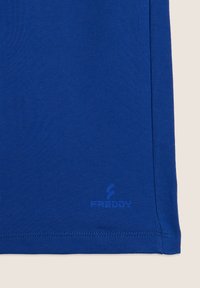 Top deportivo de algodón azul con un acabado texturizado. Presenta un pequeño logotipo "FREDDY" cerca del dobladillo. Diseño simple y ajustado con un color sólido.