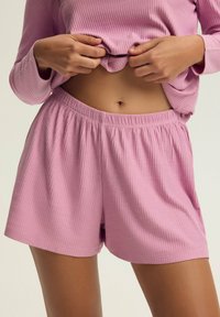 Jasnoróżowe szorty z prążkowanego materiału z elastycznym paskiem w talii, w zestawie z dopasowaną bluzą z długim rękawem. Tkanina wydaje się miękka i lekka.