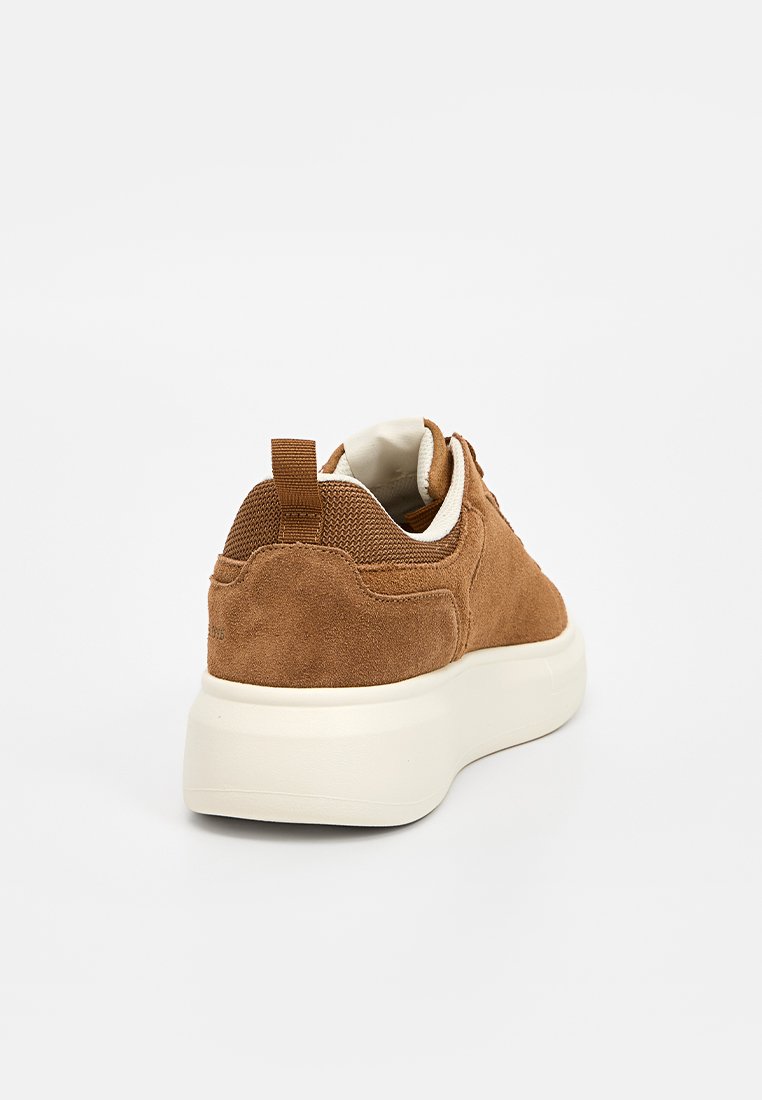 Sneaker in suede marrone con suola in gomma bianca e un accento in rete. Presenta una linguetta sul tallone e un design minimalista.
