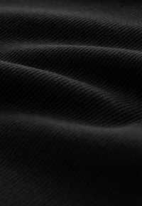 Sort ribstrikket stof med tekstureret, bølget overflade. Close-up viser fine linjer og jævne folder, der fremhæver stoffets dybde og bevægelse.