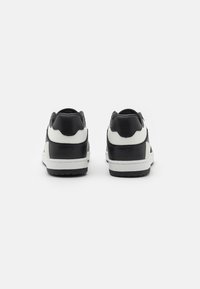 Sneaker bianco e nero con tomaia in pelle testurizzata, colletto imbottito e suola in gomma bianca con un motivo di battistrada grip.