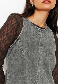 Robe en denim gris avec un corps ajusté et un col rond, associée à un haut à manches longues noir à motifs. Présente des détails de couture visibles.