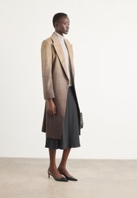 Bruine ombre wollen jas met een getailleerde pasvorm, notched lapels, gecombineerd met een grijze coltrui, zwarte satijnen rok en zwarte puntige hakken.