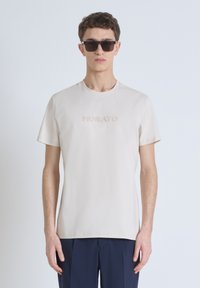 Camiseta de algodón color beige claro con cuello redondo y mangas cortas, que presenta la palabra "MORATO" en un diseño sutil y tonal.