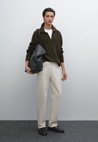 Pullover in maglia verde scuro con colletto ampio, t-shirt bianca sotto, pantaloni beige e borsa in pelle nera; texture liscia, vestibilità rilassata.