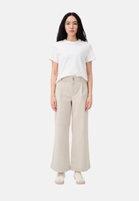 Beige wijde broek met een platte voorkant en subtiele plooidetails, gecombineerd met een effen wit T-shirt en lichtgekleurde sneakers.