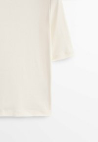 Lyhythihainen, kermavärinen T-paita, joka on valmistettu pehmeästä kankaasta. T-paidassa on yksinkertainen, suora leikkaus ja sileä pinta. Ei näkyviä kuvioita tai yksityiskohtia.