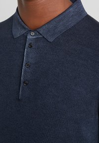 Navyblaue Polohemd aus strukturiertem Stoff mit kragenförmigem Ausschnitt und fünf schwarzen Knöpfen entlang der Knopfleiste.