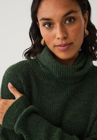 Mørkegrøn turtleneck sweater med et blødt, struktureret strik. Har lange ærmer med ribbede manchetter og en foldet krave.