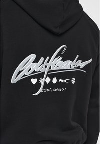 Felpa nera con cappuccio che presenta un grande grafico argentato lucido sul retro con testo e quattro simboli: cuore, diamante, fiamma e fiocco di neve.