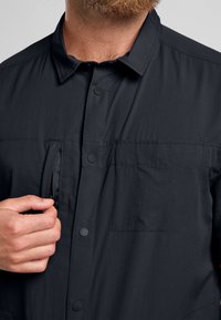 Zwarte lichtgewicht button-up shirt met een textuurstof, een vo zak en een ritssluiting detail. Voorzien van zichtbare drukknoopsluiting en een puntige kraag.