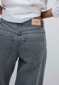 Graue Jeans aus Denim mit hoher Taille, ausgestattet mit zwei Gesäßtaschen, dezenten Steppnähten und einem hellbraunen Leder-Logoetikett am Bund.