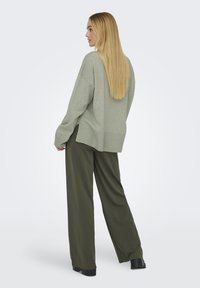 Suéter verde claro de gran tamaño con dobladillo acanalado, combinado con pantalones holgados en verde oliva y zapatos de plataforma negros, visto desde atrás.