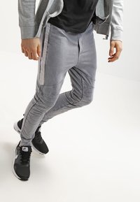 Šedé joggingové kalhoty s texturovaným prošitím a slim fit. V kombinaci s černými sportovními teniskami s bílými akcenty.