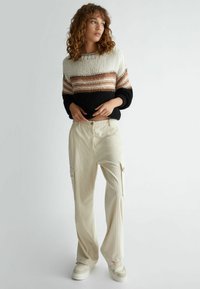 Maglione lavorato a maglia con strisce orizzontali nei colori crema, marrone e nero; abbinato a pantaloni cargo larghi color crema con tasche laterali.