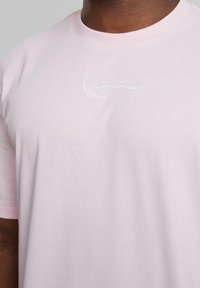Light pink cotton t-shirt featuring a round neckline and short sleeves, with a white embroidered logo on the chest area.
