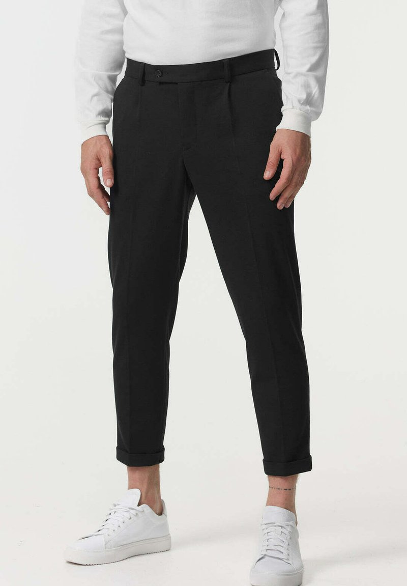 Pantaloni negri cu o croială ajustată, având un față plată, manșete rulate și o textură fină, asortați cu adidași albi.