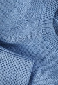 Pull bleu clair en maille avec un col rond, des bords côtelés et une texture douce avec des motifs de points distincts.