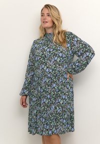 Vestido floral con cuello alto, mangas largas abullonadas y falda en capas. Presenta una base negra con patrones en azul, verde y blanco.