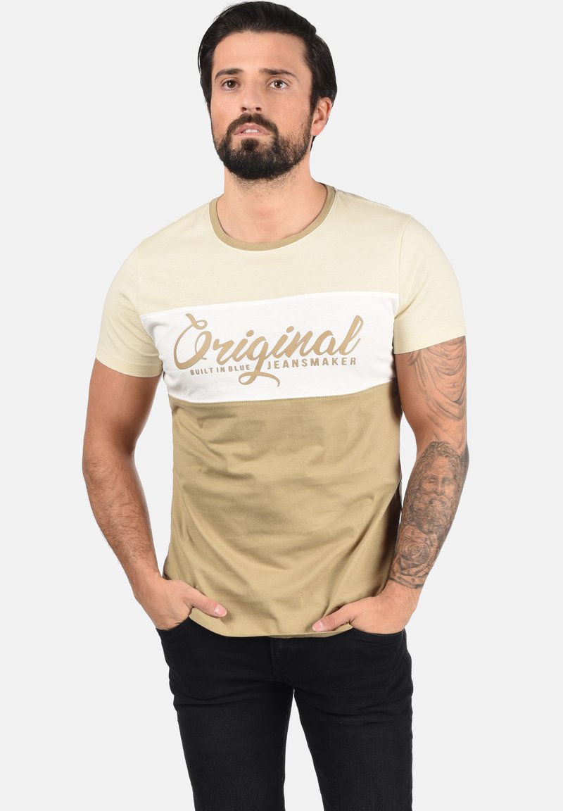 Majica kratkih rukava u bež i krem boji, s velikim grafičkim natpisom "Original Jeansmaker", okruglim izrezom i prilagođenim dizajnom.