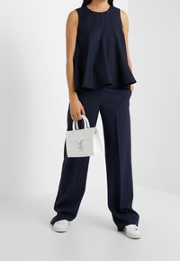 Marinblå ä sleeveless topp med en utställd design, parat med marinblå byxor. En liten vit handväska hålls, med en dekorativ charm.