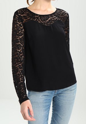 T-shirt noir à manches longues en dentelle, avec un col rond et un tissu corporel lisse. La dentelle présente un motif floral et une texture semi-transparente.