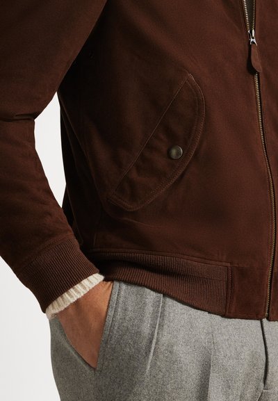 Rjava bomber jakna z gladko teksturo, z zadrgo in stranskimi žepi z zaponkami. Rebrasti manšeti in spodnji rob. Vidna podloga iz volnene mešanice.