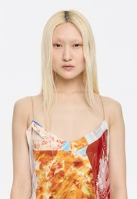 Satijnen camisole met meerkleurige abstracte bloemmotieven, dunne spaghettibandjes en een V-halslijn. Lichte en vloeiende stof.