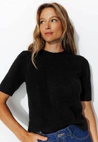 Pull noir à manches courtes en matériau doux, avec un décolleté rond et une coupe décontractée, assorti à un jean bleu.