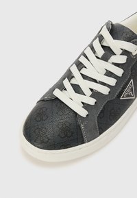 Gray sneaker featuring a textured upper with a tonal logo pattern, white laces, and a contrasting white rubber sole.