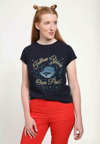 Marineblå bomulds T-shirt med et grafisk design af et katteagtigt dyr med solbriller og teksten "Følg din egen vej." Sammen med røde bukser.
