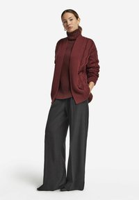 Mörkröd kabelstickad kofta lager på lager över en matchande polokrage, i kombination med vida gråsvarta byxor. Slät textur och avslappnad passform.