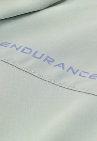 Lichtgroene stof met een rasterstructuur en zichtbare stiksels, met het woord "ENDURANCE" in het blauw.