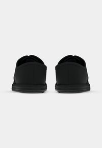 Et par svarte sneakers sett bakfra, som viser hælene og sålene på en hvit bakgrunn.