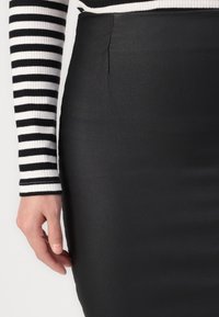 Jupe crayon noire avec une texture lisse, dotée d'une couture latérale et d'une taille haute. Associée à un haut à manches longues rayé noir et blanc.