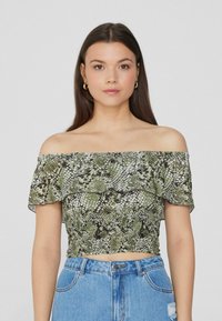 Top corto off-the-shoulder con stampa serpente. Caratterizzato da un collo arricciato, colori verde e nero, e un design aderente. Abbinato a jeans a vita alta.