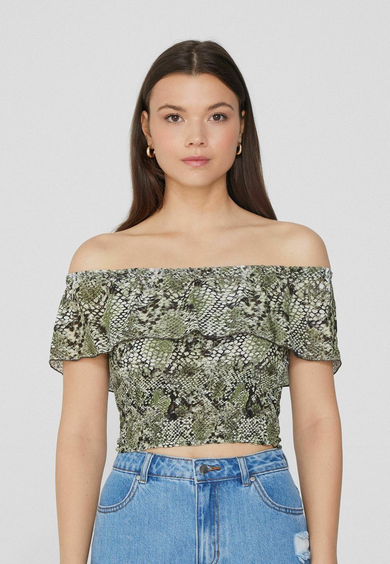 Top corto off-the-shoulder con stampa serpente. Caratterizzato da un collo arricciato, colori verde e nero, e un design aderente. Abbinato a jeans a vita alta.