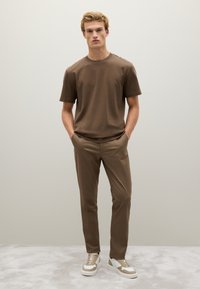 Braun leichtes T-Shirt und maßgeschneiderte Hose, kombiniert mit weißen und beigen Sneakers, mit glatter Textur und schlichter Gestaltung, vor einem neutralen Hintergrund.