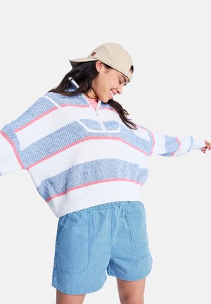 Grob gestrickter Pullover mit blauen, weißen und pinken Streifen; verfügt über einen halben Reißverschluss am Kragen. Kombiniert mit hellblauen gestreiften Shorts.