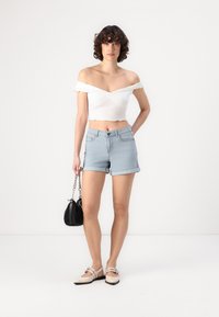 Biela crop blúzka bez ramienok s volánikmi, spárovaná so svetlomodrými džínovými šortkami. Model má malú čiernu kabelku a na nohách béžové baleríny.