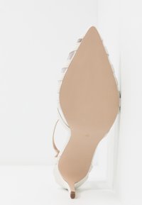 Escarpin blanc à talon kitten pointu avec semelle texturée et panneaux latéraux en maille, photographié par la semelle sur fond blanc.