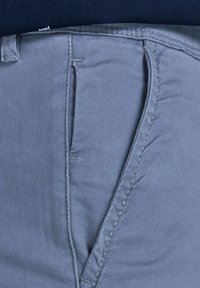 Gros plan d'une poche de pantalon bleu clair avec coutures visibles et ceinture sur un fond bleu foncé.