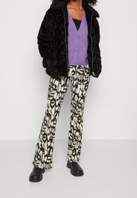 Chaqueta de piel sintética negra, suéter morado de botones, pantalones acampanados negros y crema con estampado, y botas negras gruesas.